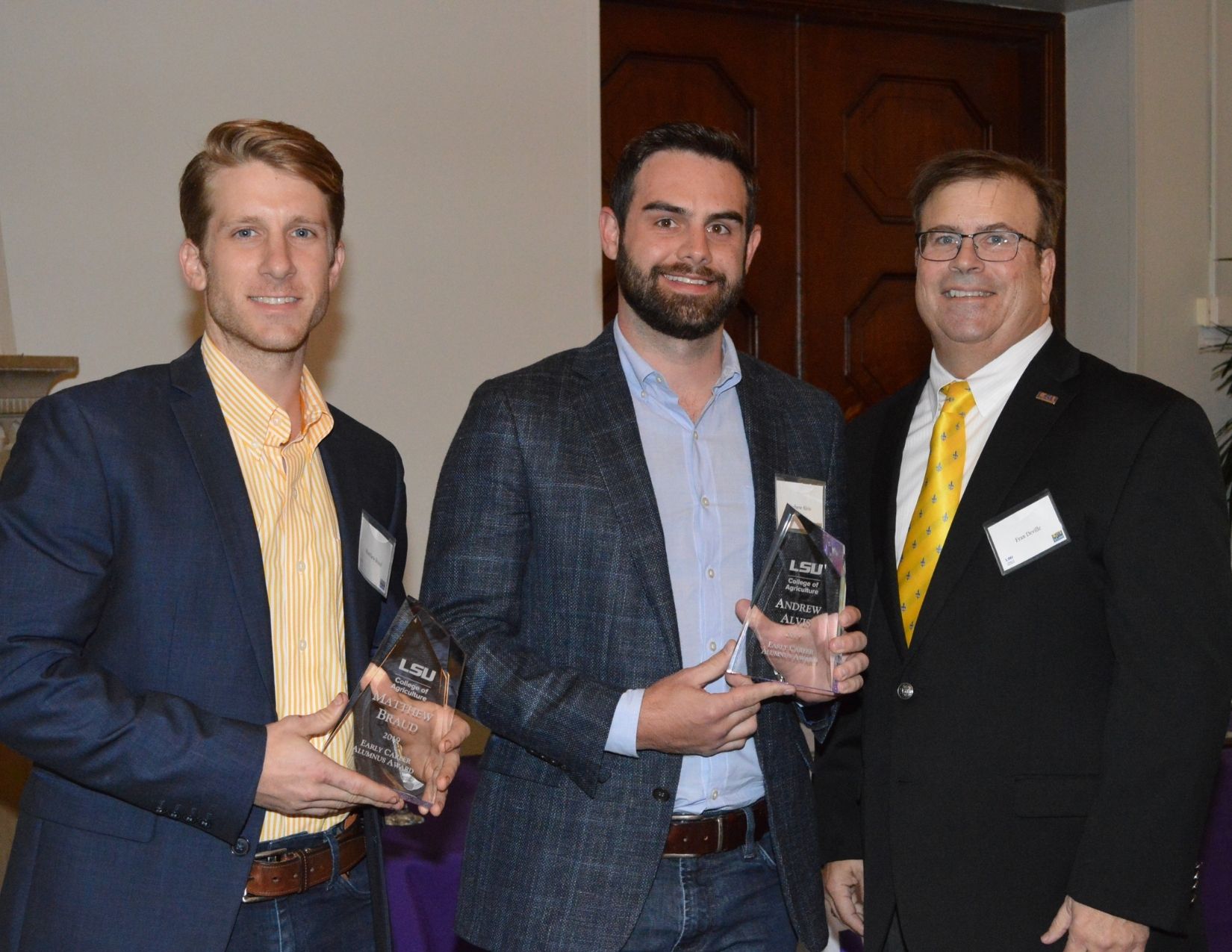 Three people pose for picture, two hold awards