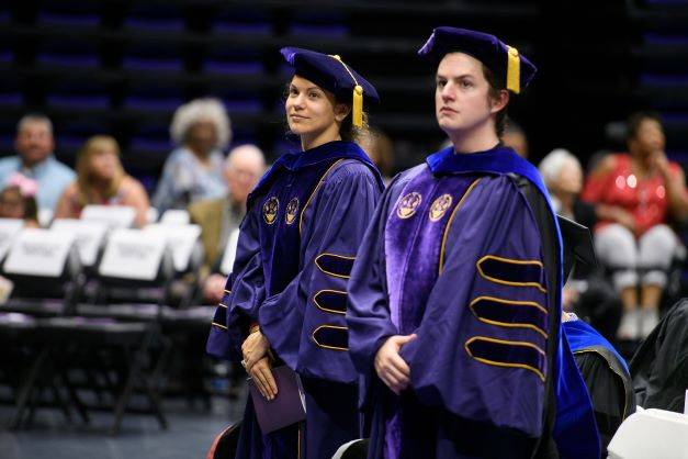 two PhD candidates in regalia at a graduation ceremony