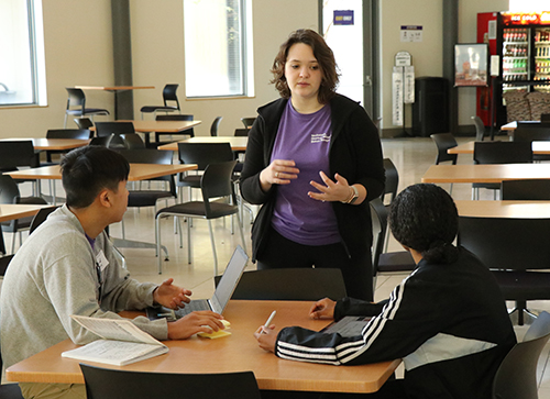 female standing and talking to two seated students