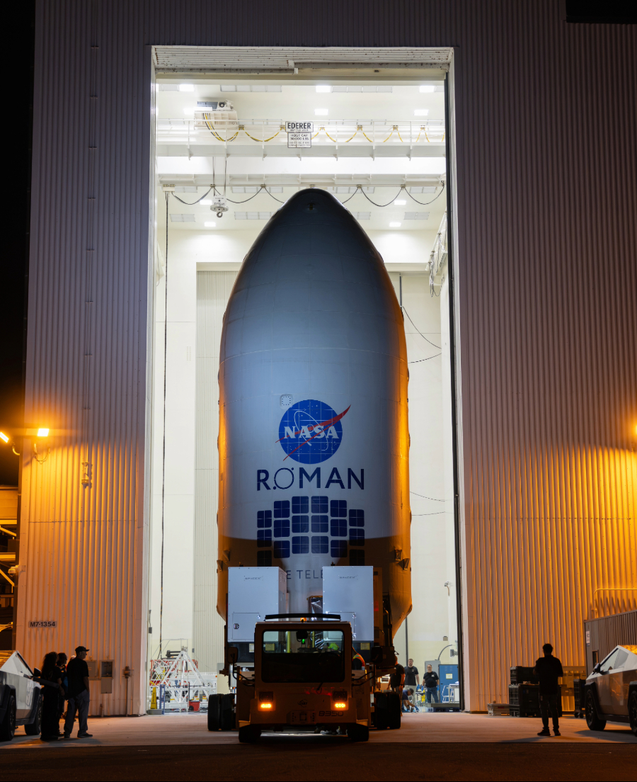 Nancy Grace Roman Space Telescope enclosed in a white payload fairing and transported on a large platform at Kennedy Space Center.